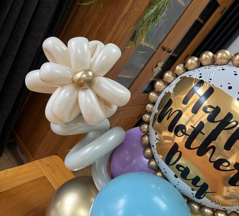 A decorative arrangement featuring a balloon flower and a "Happy Mother’s Day" sign.