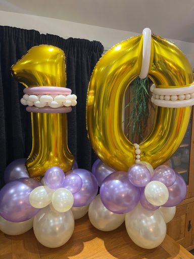 Golden number "10" balloons atop a decoration of purple and white balloons.
