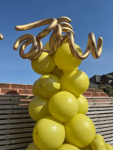 A tower of yellow balloons topped with a golden, curled decoration.