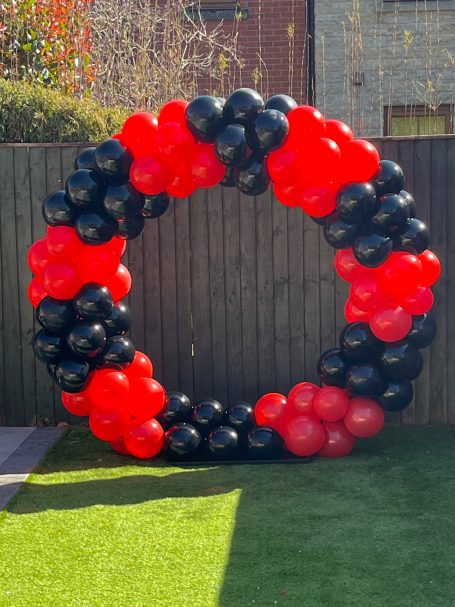A circular arrangement of red and black balloons against a grass background.