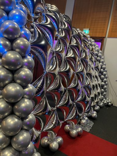 Decorative arch made of silver and metallic balloons in a vibrant event setting.