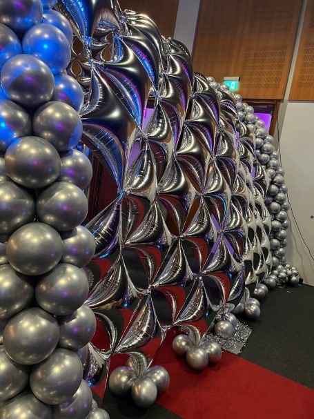 A decorative backdrop made of silver balloons arranged in a swirling pattern.