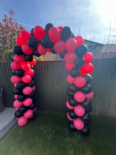 Decorative arch made of red, pink, and black balloons in an outdoor setting.